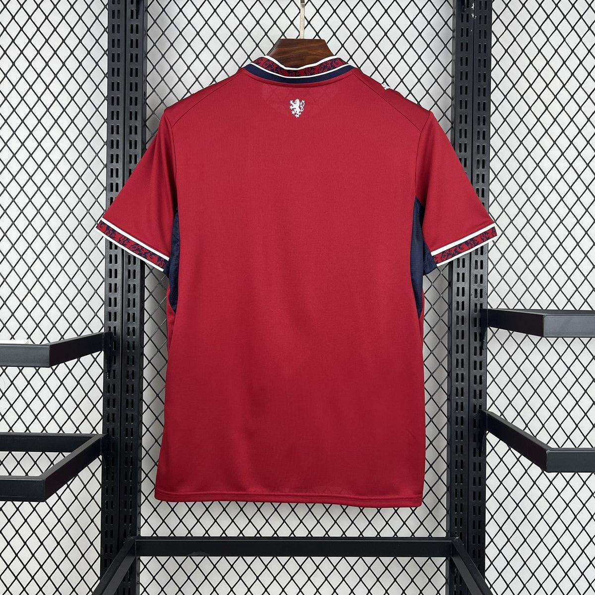 Red sports jersey with a logo on the chest, hanging against a black metal fence.