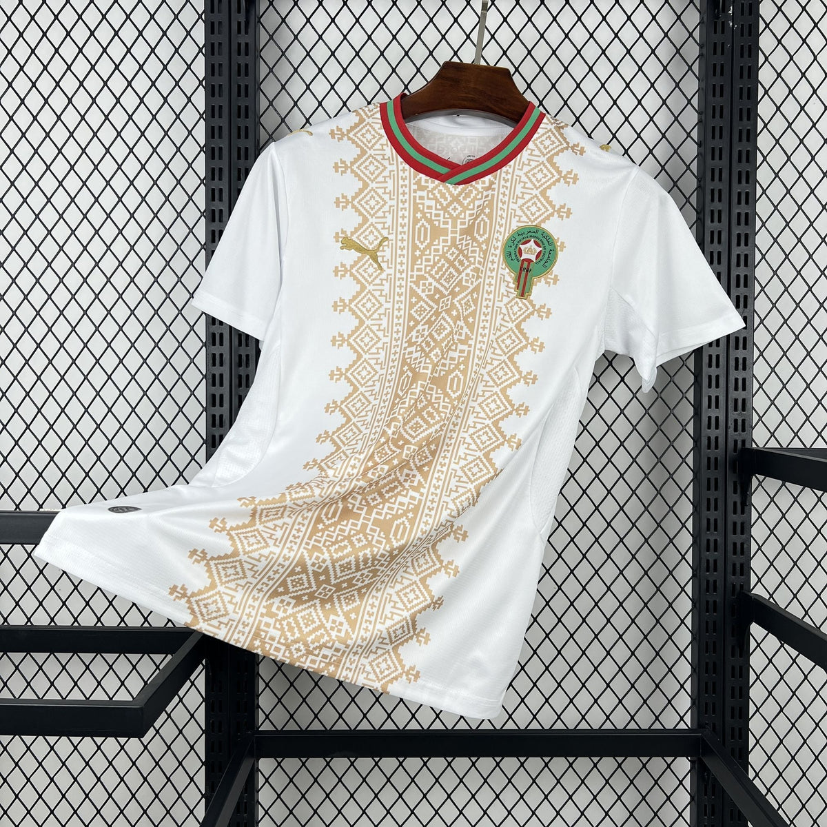 White t-shirt with gold patterns and a green emblem on a black metal rack.