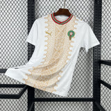 White t-shirt with gold patterns and a green emblem on a black metal rack.