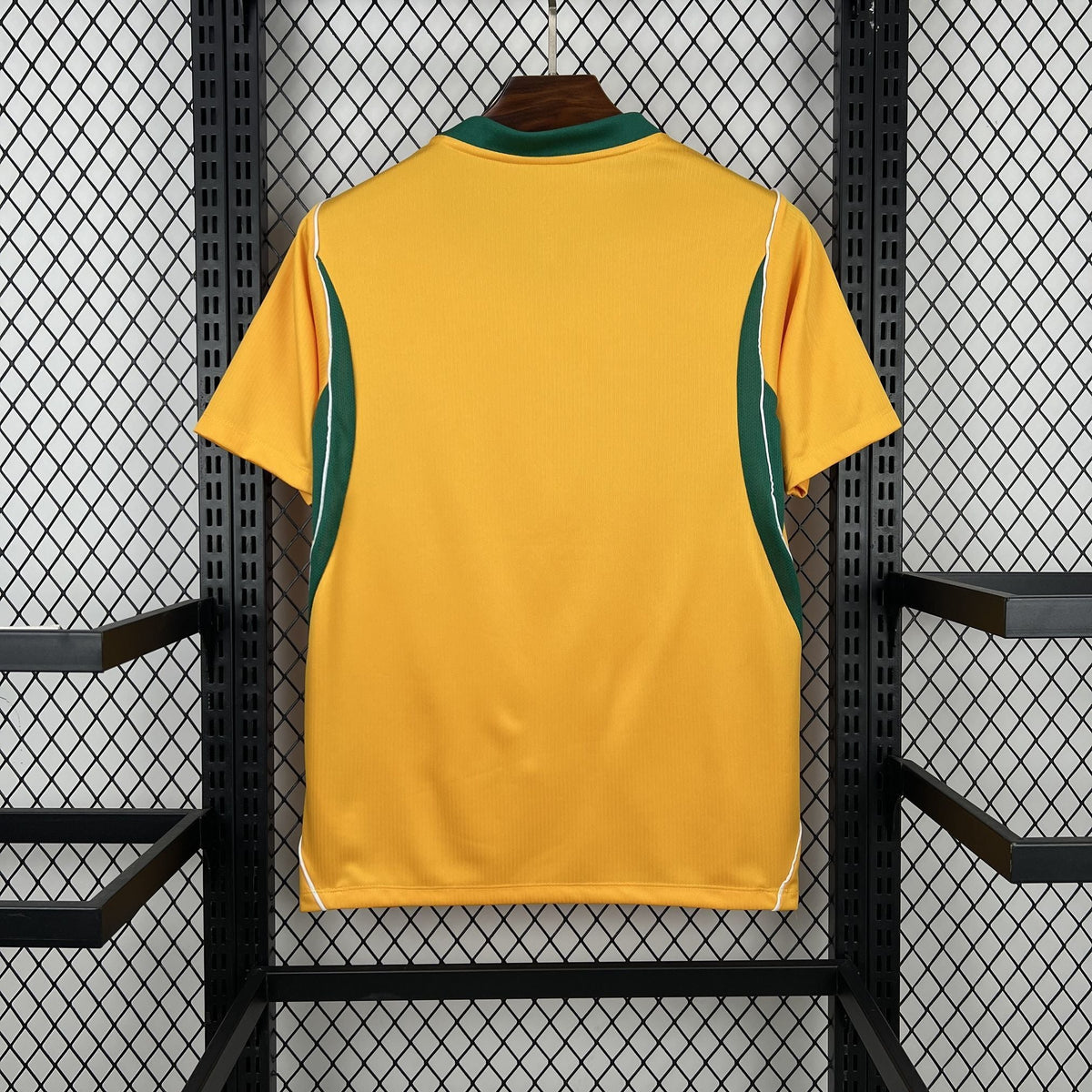 Yellow sports jersey with green accents on a hanger against a black metal fence background