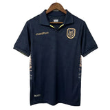 Navy blue sports shirt with logos on a hanger against a light gray background